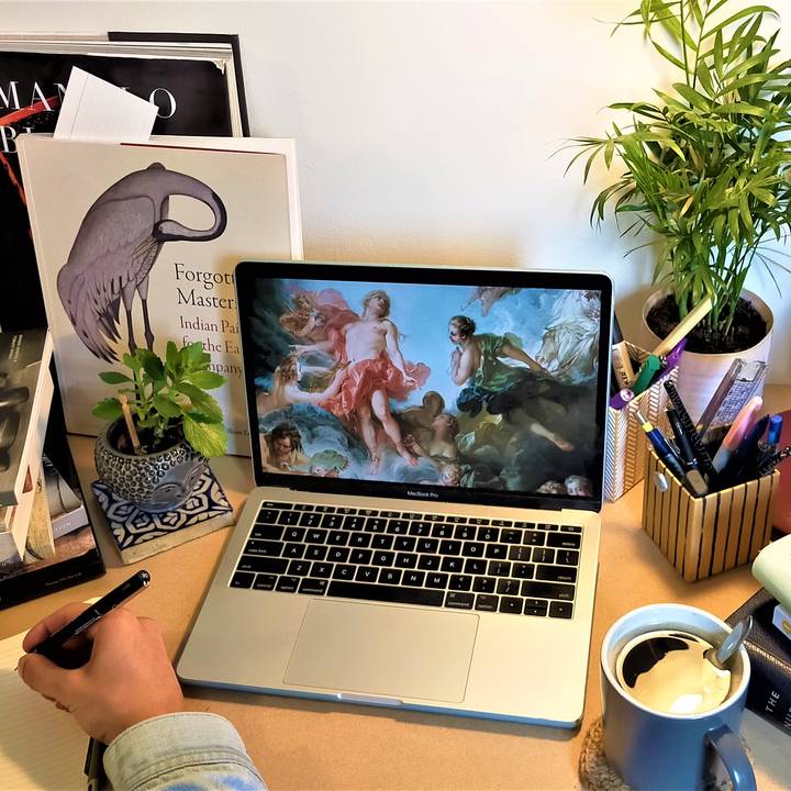 Person writing at desk with laptop and books on